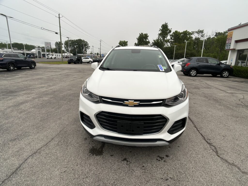 Front view of a white Chevrolet SUV in a parking lot with other cars and dealership buildings in the background
