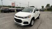 White Chevrolet SUV in the foreground at a car dealership lot, with other vehicles and an EZ LOAN sign in the background