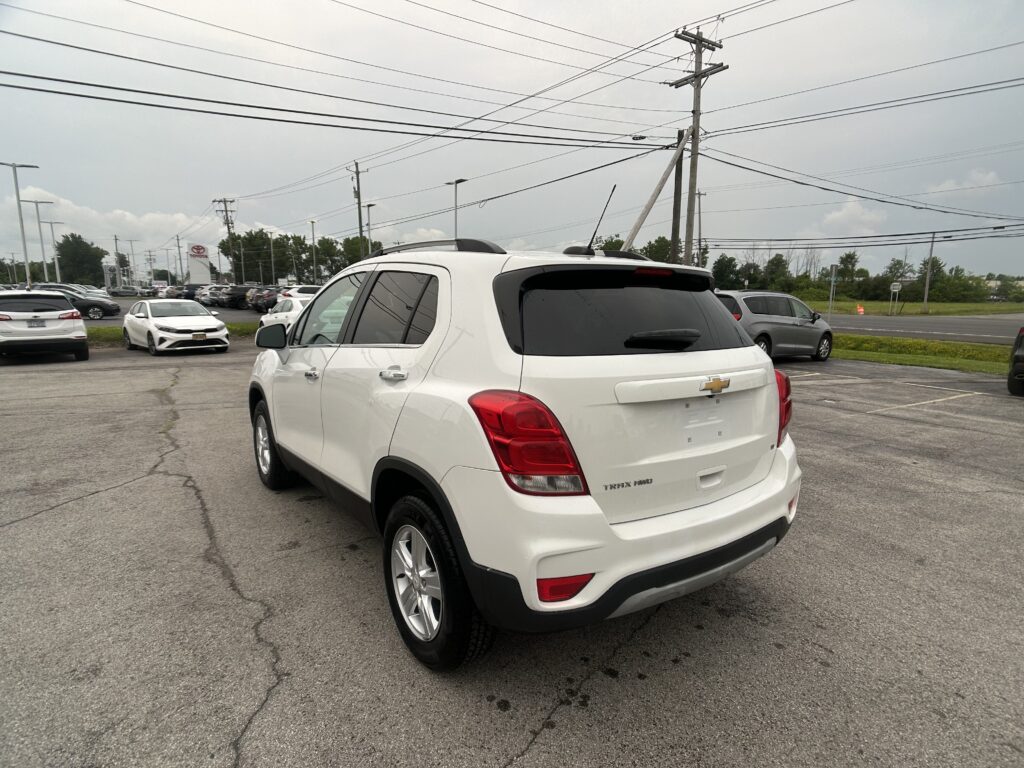 White Chevrolet SUV seen from the rear side in a busy dealership parking lot with other cars and overhead power lines.