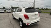 White Chevrolet SUV seen from the rear side in a busy dealership parking lot with other cars and overhead power lines.
