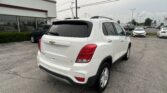 White Chevrolet SUV seen from the rear in a car lot next to a dealership building with other vehicles in the background.