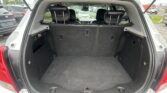 Open SUV cargo area with rear seats upright, showing a spacious black carpeting and side panels, parked lot visible outside.