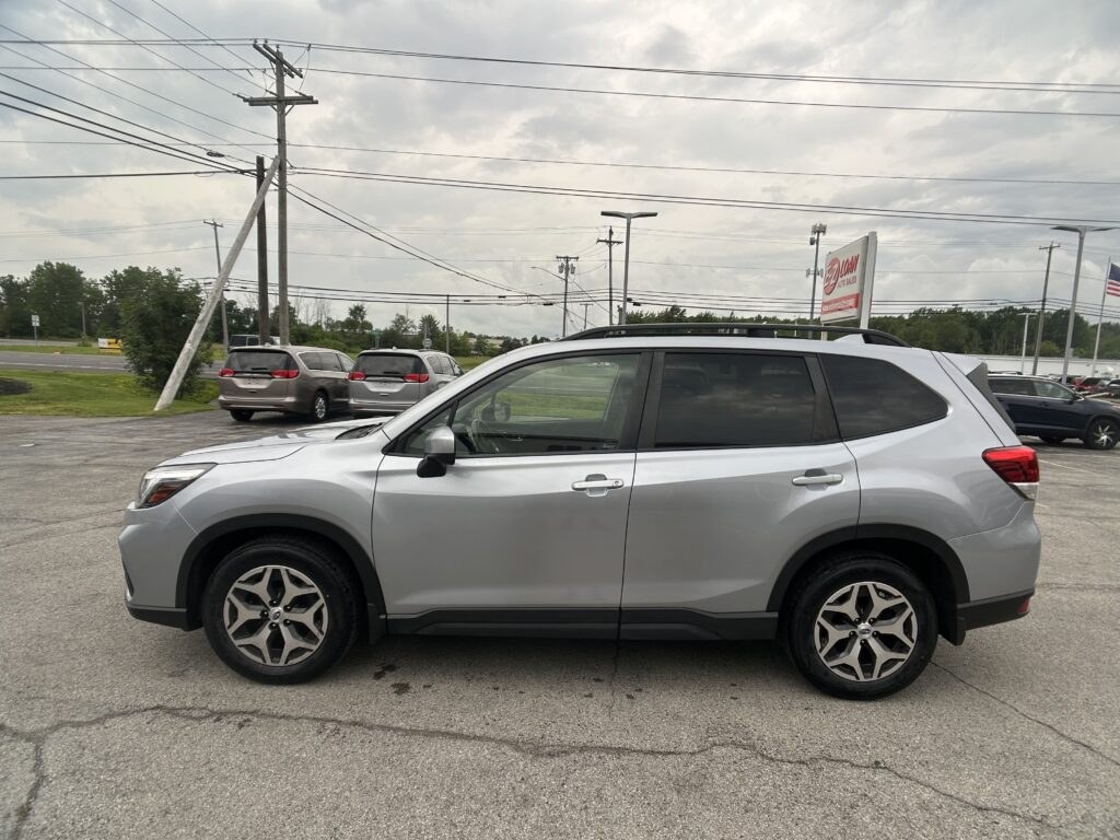 Silver SUV in a dealership parking lot with other vans nearby and power lines overhead against a cloudy sky.