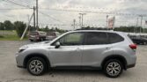Silver SUV in a dealership parking lot with other vans nearby and power lines overhead against a cloudy sky.