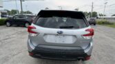 Rear view of a silver Subaru Forester in a parking lot with other vehicles and power lines overhead, light rain on the rear window.