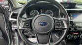 Leather steering wheel centered in the cockpit with analog gauges and a right-side touchscreen display, view of a parking lot through the windshield