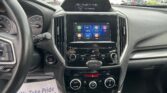 Driver's view of a car interior: center touchscreen displaying apps, surrounding climate controls, and instrument cluster to the left of the steering wheel.