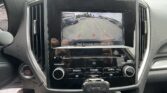 Infotainment screen showing a rear-view camera feed with green/yellow/red guidelines in a parking lot; caution text at bottom says 'Check Surroundings Before Backing Up'