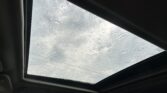 View through a car's panoramic sunroof with raindrops on the glass and a cloudy sky outside.