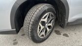 Close-up of a silver SUV's front wheel and tire, showing a multi-spoke alloy rim and tread detail with a muddy wheel well.