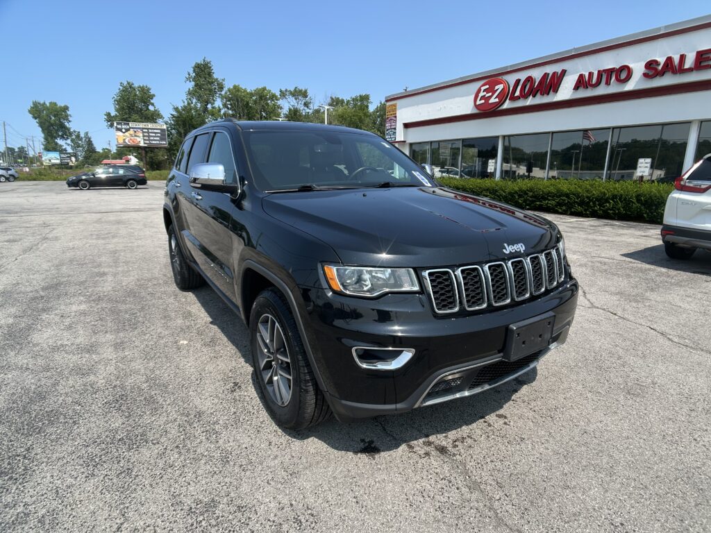 Black Jeep SUV in a dealership lot with a white building and red E-Z LOAN AUTO SALES sign.