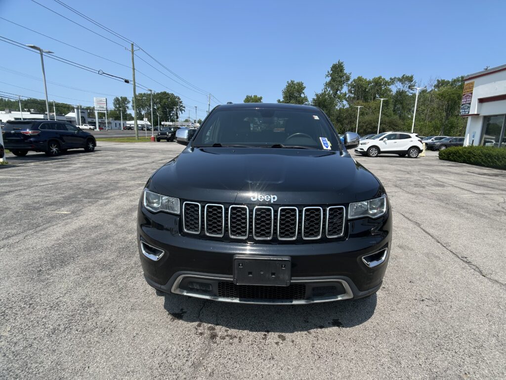 Front view of a black Jeep SUV in a parking lot with other cars and a clear blue sky above.