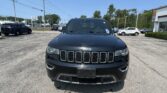 Front view of a black Jeep SUV in a parking lot with other cars and a clear blue sky above.