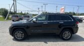 Black Jeep Grand Cherokee SUV parked in a car lot with other vehicles and a showing sign in background reading 'Auto Sales'