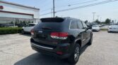 Rear view of a black Jeep SUV (Limited) parked in a car dealership lot near a white building with large windows and power lines overhead.