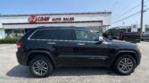 Black SUV parked in front of a white auto sales storefront with red sign reading 'E-Z LOAN AUTO SALES' and other vehicles in lot under a clear blue sky.
