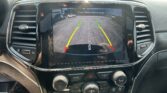 Car infotainment screen showing rear-view camera with green/yellow/red guiding lines and 'Check Entire Surroundings' message.
