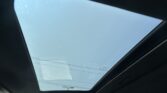 Blue sky visible through an open panoramic sunroof in a car, with dark interior surrounding the glass panel.