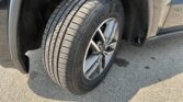 Close-up of a car tire on a silver alloy wheel, with the wheel well and fender in view on a paved surface.