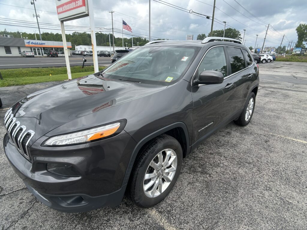 Front-left view of a gray SUV parked on an asphalt lot with a Quick Lane storefront and an American flag in the background.