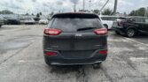 Rear view of a dark gray Jeep Grand Cherokee Limited 4x4 in a crowded parking lot, with other SUVs and cars around and power lines overhead.