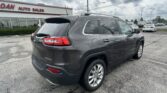 Gray SUV parked in front of a dealership with 'AUTO SALES' sign, showing rear and passenger side with roof rails.