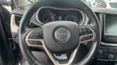 Driver's view of the Jeep steering wheel and instrument cluster with the center console and touchscreen on the right, in a dealership lot outside the car