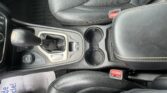 Close-up of a car's center console with gear shifter, cup holder, and black leather seats with contrast stitching.