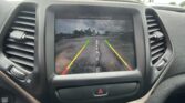 In-car display showing a rearview camera view with colored guiding lines (green, yellow, red) and the message 'Check Entire Surroundings' at the top.
