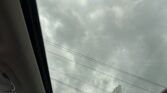 View through a car's panoramic sunroof of a gray, cloudy sky with power lines outside the vehicle window, roadside scene below.