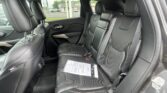 Rear passenger area of a black leather SUV with two captain chairs, seat belts fastened and papers on the seat; outside street scene visible through the windows.