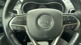 Close-up of a Jeep steering wheel with left and right control buttons and the instrument cluster in the background.