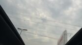 View through the car's panoramic sunroof showing a cloudy gray sky and power lines, with a parking lot and buildings visible outside.