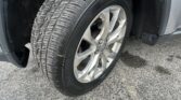 Tire and alloy wheel of a vehicle parked on asphalt, with visible tread pattern and part of the wheel well.
