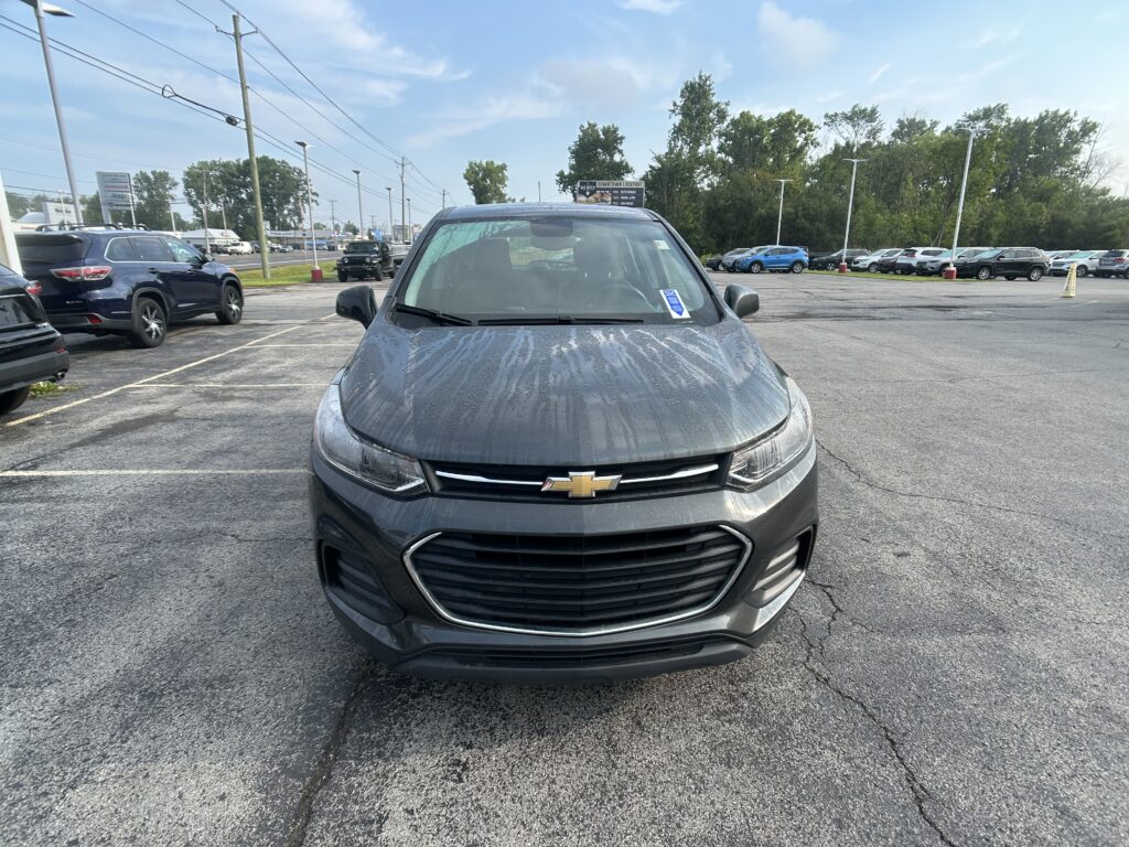 Front view of a gray Chevrolet SUV parked in a busy car lot with other vehicles and power lines in the background, blue sky overhead.