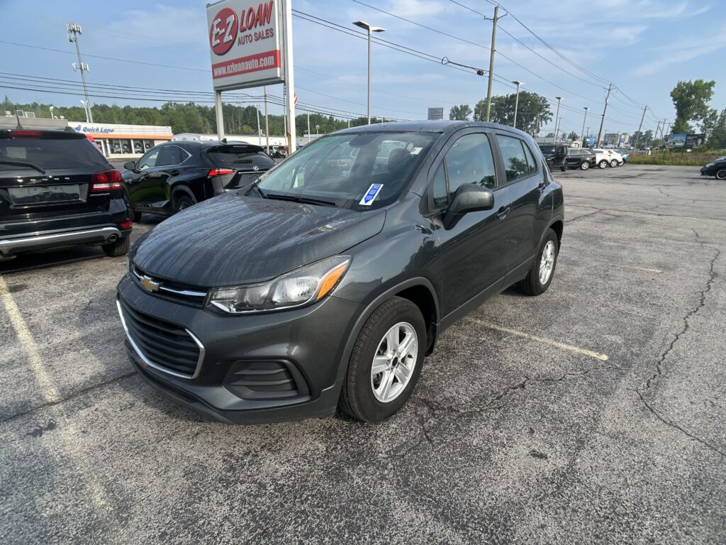 Gray Chevrolet SUV in a car dealership lot, with other vehicles and a tall EZ LOAN sign in the background.