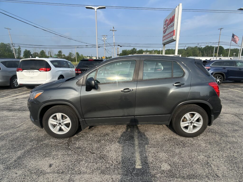 Gray SUV parked in a crowded car lot with other vehicles and a tall auto sales sign in the background.
