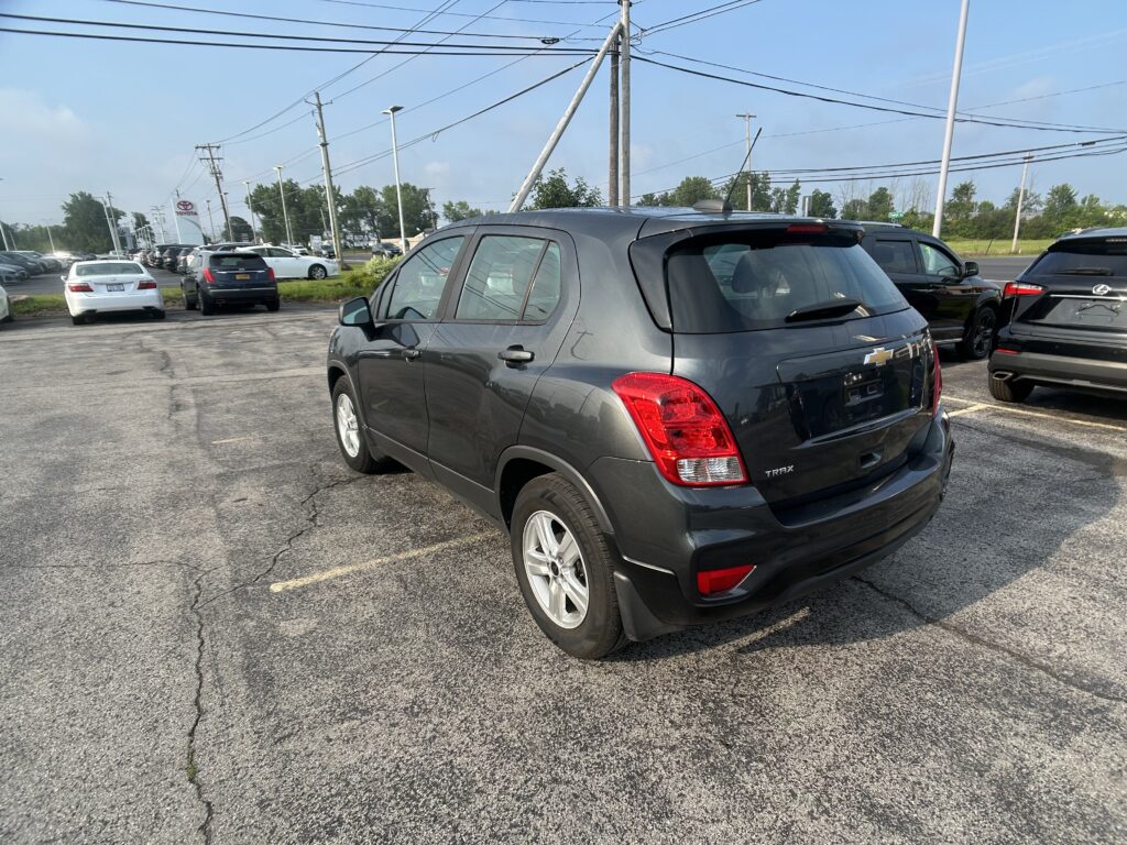 Gray Chevrolet Trax in a car dealership lot with other vehicles and overhead power lines visible under a blue sky