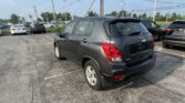 Gray Chevrolet Trax in a car dealership lot with other vehicles and overhead power lines visible under a blue sky