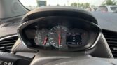 Inside a car cockpit showing the steering wheel, speedometer and dashboard with outdoor traffic visible through the windshield.