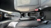 Front interior of a car showing the center console and front seats, with the gear shifter on the left and two cup holders in the middle. A red seat belt buckle is visible on the right side of the seat.