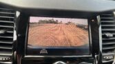 In-dash infotainment screen showing the car’s rear-view camera feed with yellow parking guide lines in a parking lot.