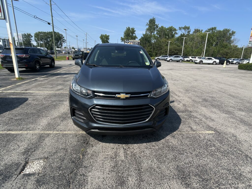 Front view of a gray Chevrolet SUV parked in a dealership lot on a sunny day, with rows of cars and power lines in the background.