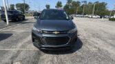 Front view of a gray Chevrolet SUV parked in a dealership lot on a sunny day, with rows of cars and power lines in the background.