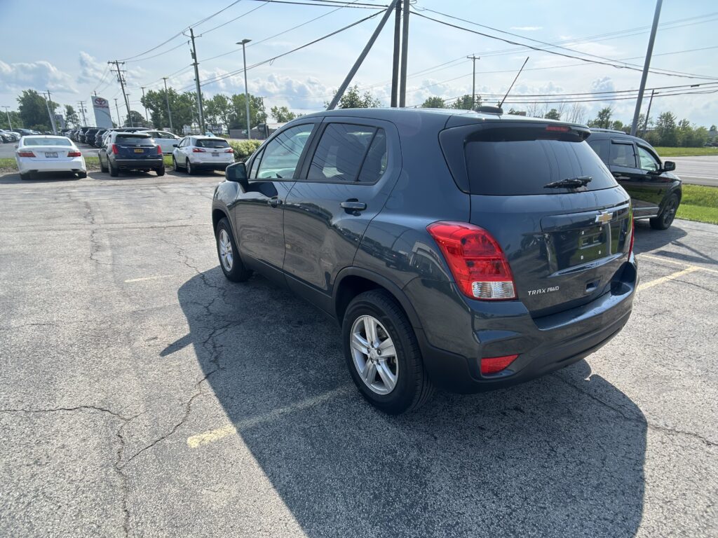Rear three-quarter view of a dark blue Chevrolet Trax SUV parked in a car lot, with other cars and a Toyota dealership sign visible in the background.