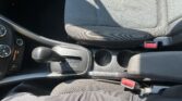 View of a car's front interior: driver and passenger seats, center console, gear shifter, cup holders, and red seatbelt buckles visible.