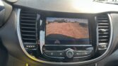 Car dashboard touchscreen displaying rear-view camera feed with parking guidelines in a parking lot