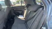 Back seat of a car with black fabric upholstery and visible seat belts, view of a parking lot through the windows.