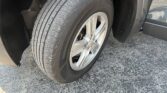 Close-up of a car tire and silver alloy wheel, with the wheel well and fender in view on asphalt ground.