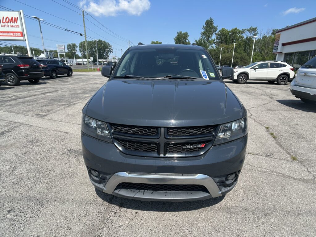 Front view of a gray Dodge SUV parked in a car dealership lot with other vehicles and a sign on the left.